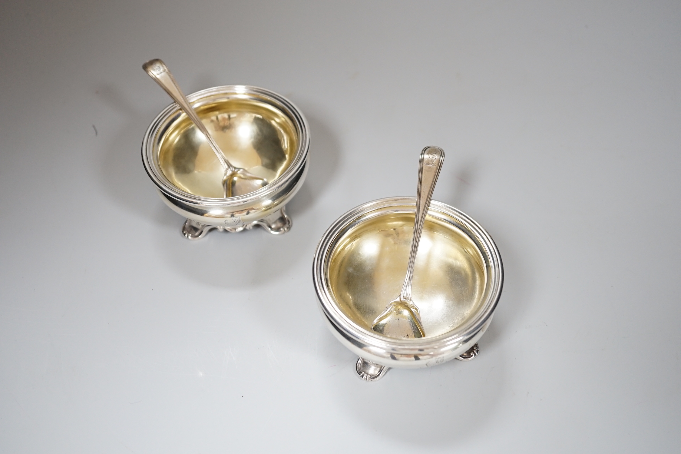 A pair of Victorian circular silver salts, with crests and scroll feet, makers Edward Barnard & Sons, London 1839, 207 grams, and a pair of George IV silver salt spoons, London 1827, 19 grams